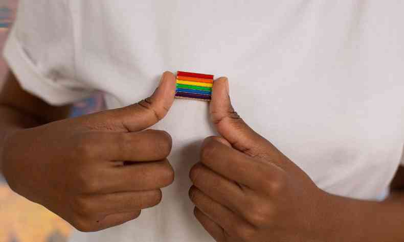 Mos de uma pessoa negra segurando um broche da Bandeira LGBT