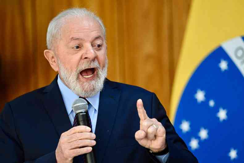 Lula com dedo em riste falando ao microfone ao lado de uma bandeira do Brasil