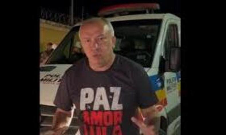 Foto retirada do vdeo mostra Paulo Guedes diante uma viatura da PM; ele usa uma camisa com os dizeres Paz, amor Lula