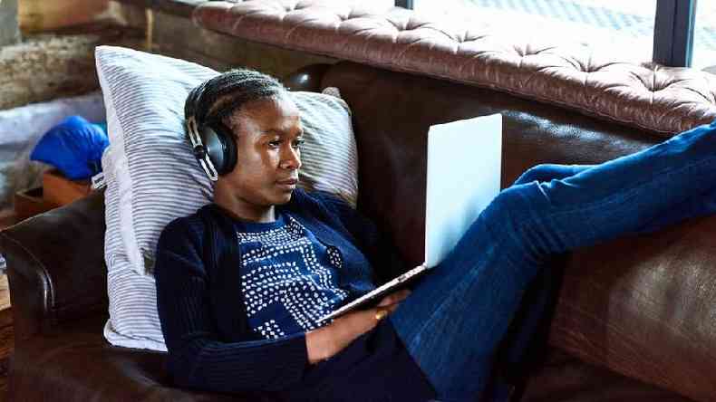 Mulher usando laptop e fones de ouvido enquanto est deitada em um sof