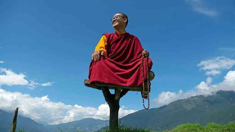 Rinpoche em um assento alto, com o cu ao fundo
