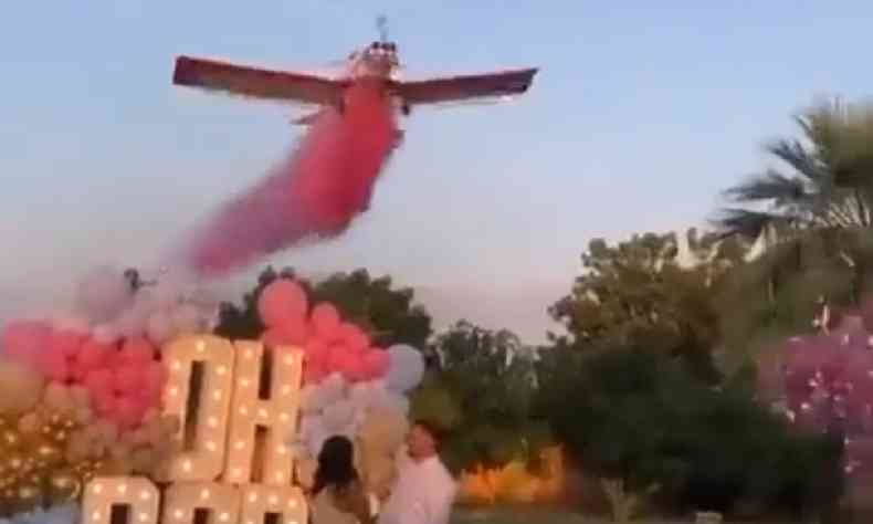 Avio de pequeno porte soltando fumaa rosa sobre um casal. Atrs do casal se v um letreiro escrito 'Oh Baby' enfeitado com bales nas cores rosa e azul