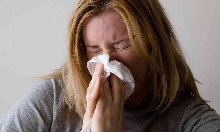 mulher de olhos fechados, com leno entre as mos e limpando o nariz diante de um quadro de gripe