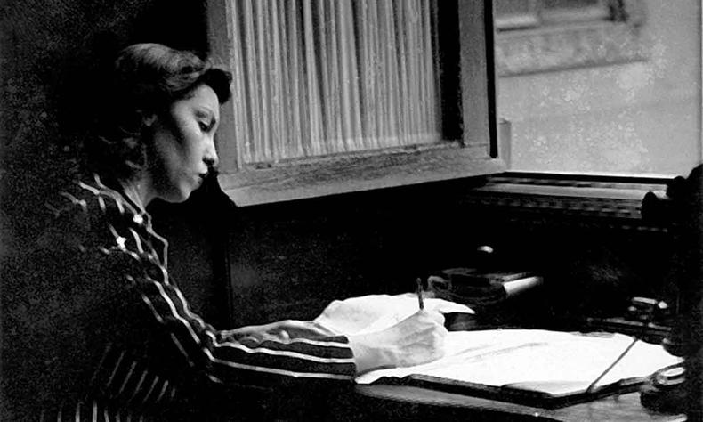 De tailleur listrado, sentada em sua escrivaninha, Clarice Lispector escreve  mo 