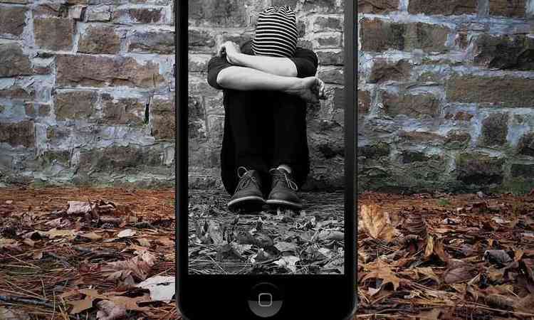 adolescente agachado, com a cabea entre as pernas visto pela tela de um smartphone