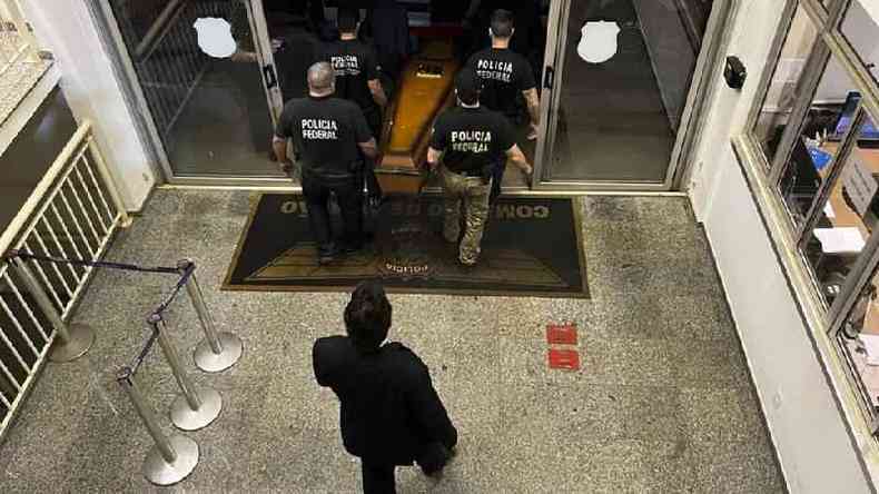 Foto tirada de um andar superior mostra agentes da Polícia Federal saindo pela porta levando caixão