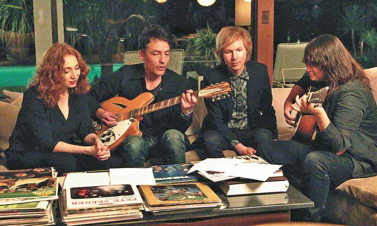 Sentados em sof, atores tocam violo e observam pilhas de vinil em cena de 'Echo in the Canyon'