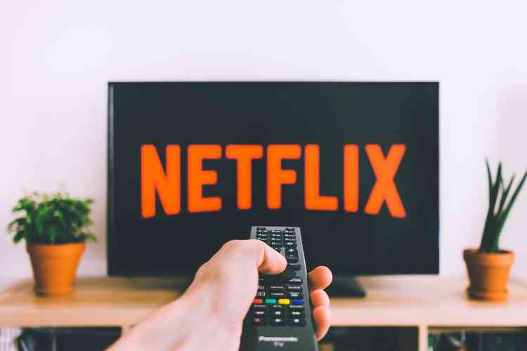 Televiso com logomarca da Netflix na tela e mo segurando controle remoto