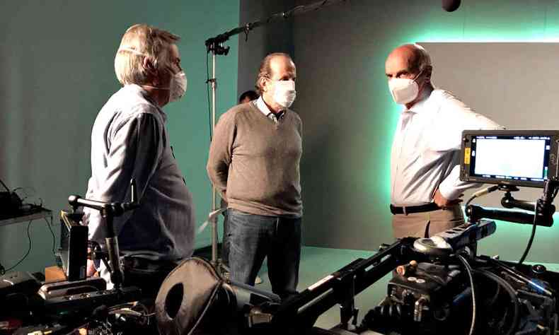 Eduardo Escorel, Lauro Escorel e Drauzio Varella, de p e suando mscara, num set de filmagens, prximos de uma cmera
