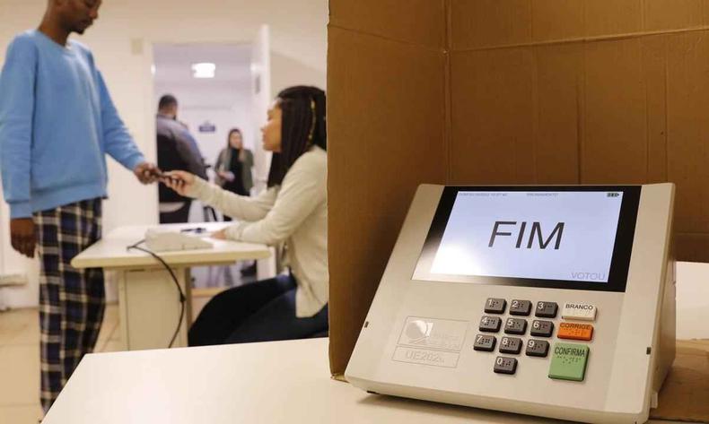 Os mesários que trabalham nas eleições são convocados ou voluntários(foto: Fernando Frazão/ Agência Brasil) Na foto, urna eletrônica marcando 'fim' e, atrás, mesário e eleitor