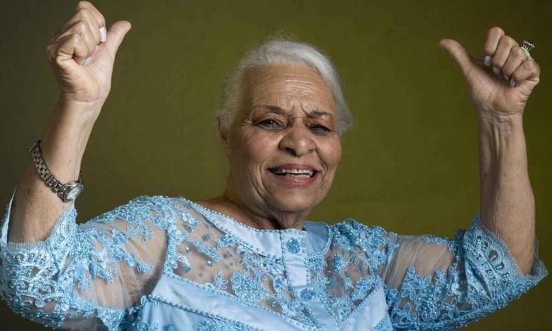 De vestido azul, sorrindo e com os braos para o alto, cantora Marclia de Queiroz Pinheiro olha para a cmera. Ela foi aprovada no programa The voice+