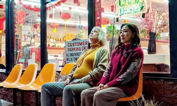 As atrizes Michelle Yeoh (Evelyn Wang) e Jamie Lee Curtis (Deirdre Beaubeirdre) sentadas lado a lado na frente de uma lavanderia em cena de 'Tudo em todo lugar ao mesmo tempo'
