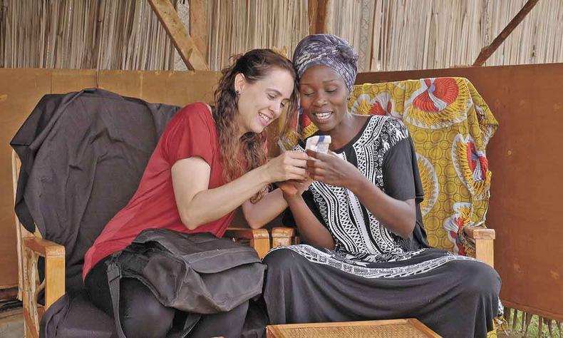 A mineira Joana Oliveira e a africana Kevin Adweko compartilham alegrias e também sofrimentos no documentário 'Kevin'(foto: Cristina Maure/divulgação ) Joana Oliveira e Kevin Adweko sorriem e olham para maço de cigarro que ambas seguram em cena do filme Kevin