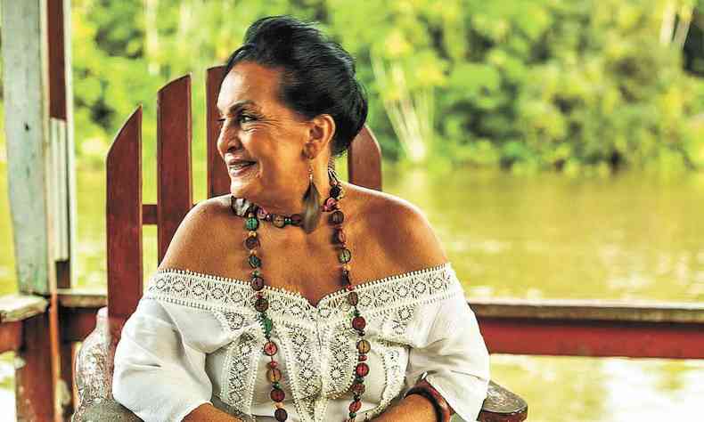 Com vestido branco de renda e colar de contas, cantora Oneide Bastos olha para o lado, tendo ao fundo rio do Amapá