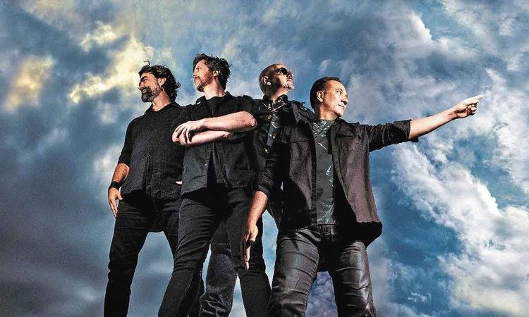 Os quatro integrantes do Biqu�ni, ao ar livre, de p�, posam para foto gesticulando para a c�mera
