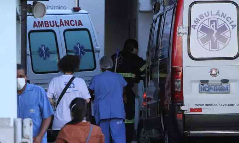 Imagem mostra quatro pessoas de costas próximas a duas ambulâncias