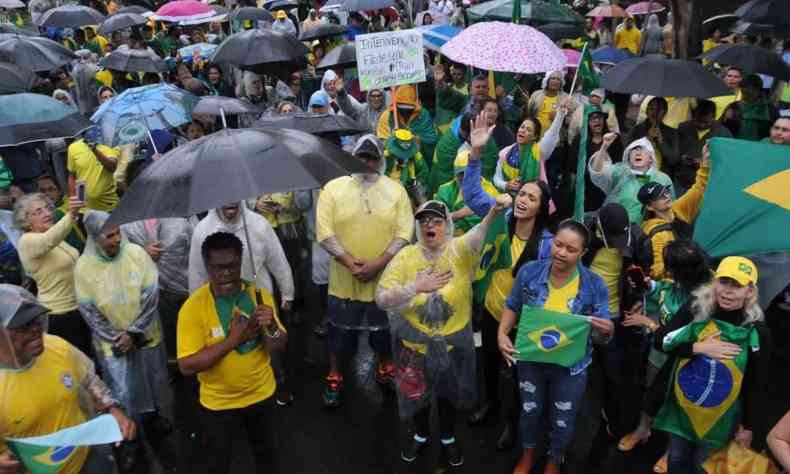 Apoiadores de verde e amarelo com guarda-chuvas e capas durante protesto em Belo Horizonte