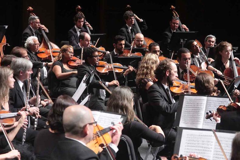 vestidos de preto, no palco, com seus instrumentos, msicos da orquestra sinfnica de minas gerais tocam durante concerto 
