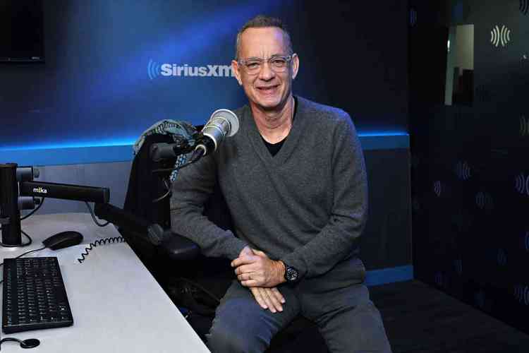 ator Tom Hanks est sentado ao lado de microfone e ri para a cmera