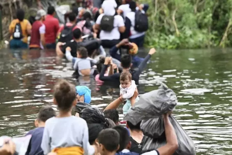 Imigrantes atravessando crrego com crianas e seus pertences