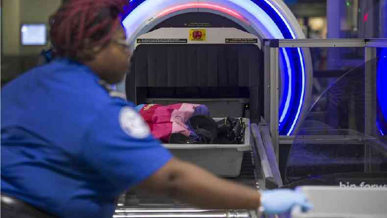 Imagem de arquivo de um funcionário da segurança do aeroporto ajudando viajantes a colocar suas malas no scanner 3D no Aeroporto Internacional de Miami em maio de 2019