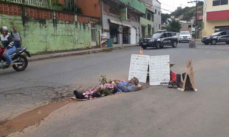 Homem, de 58 anos, ficou deitado no buraco por 4 horas(foto: Arquivo pessoal) Na foto, homem realizando protesto deitando num dos buracos das ruas de Itabira. Junto a ele, placas e flores, simulando um sepultamento