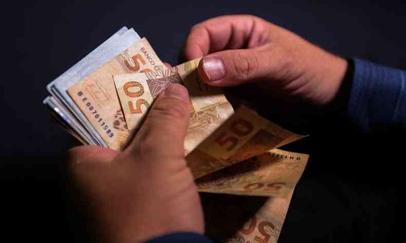 Foto mostra mos de uma pessoa com notas de 50 reais
