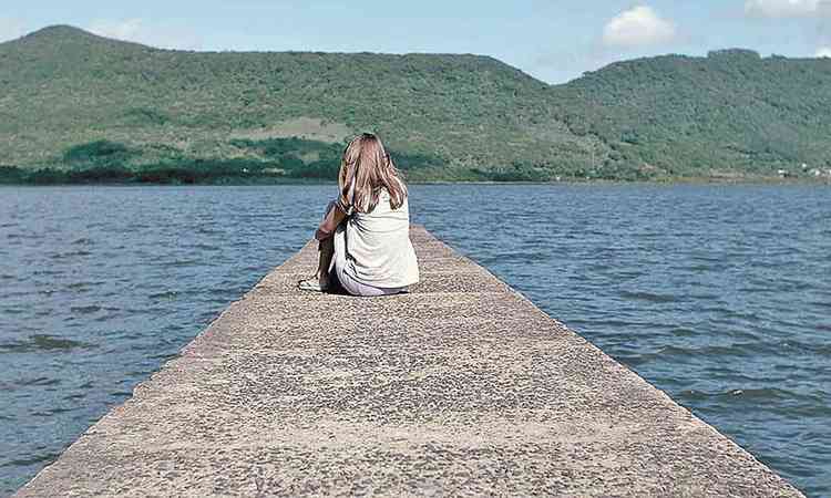 Atriz adolescente est de costas num per diante de imensa lagoa no filme A primeira morte de Joana
