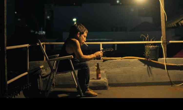 Ator est sentado em cadeira  noite, lendo algo e sob a luz do poste, em cena do filme Big band