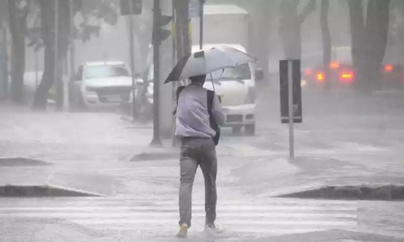 Homem de blusa e calça escura, segurando um guarda-chuva para se proteger de tempestade em BH 