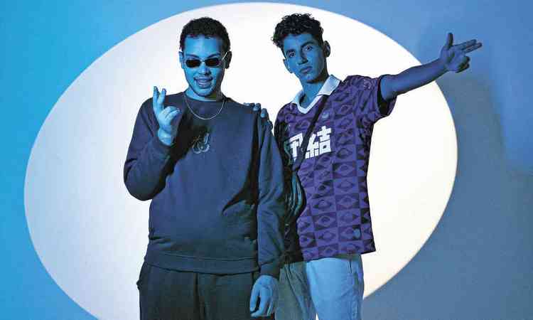 Rapper Ogoin e DJ Linguini esto em cenrio azul e olham para a cmera