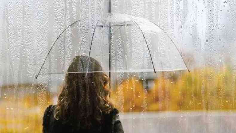 Pessoa de costas segura guarda chuva transparente em meio à chuva
