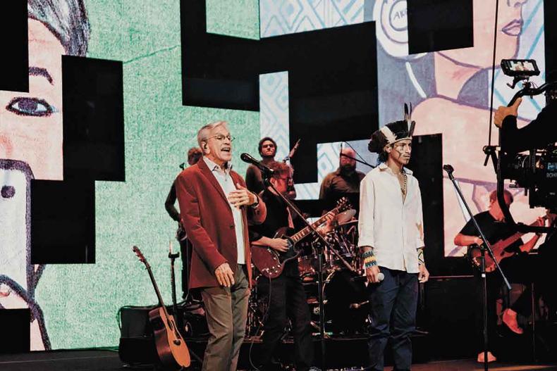 Caetano Veloso e o rapper indígena Owerá, de 20 anos, se unem na interpretação de ''Um índio'', seguida de ''Mbaraeté'' (foto: HBO Max / Dueto Filmes / Divulgação) Com a banda postada atrás de si no palco, Caetano Veloso e o rapper indígena Owerá cantam em frente aos seus respectivos microfones