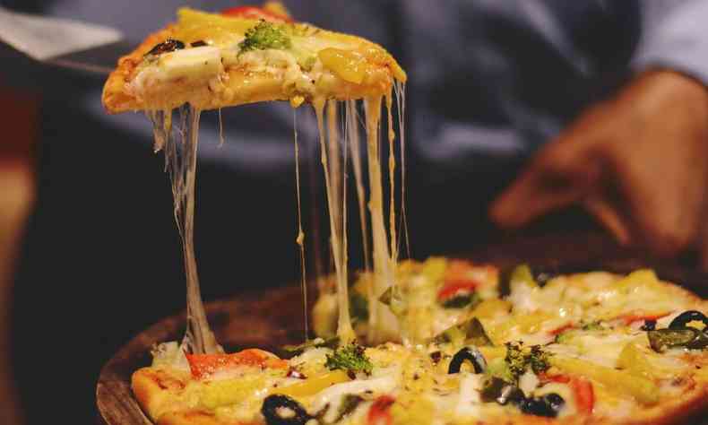 Pessoa tirando fatia de pizza de pizza em mesa com queijo derretendo