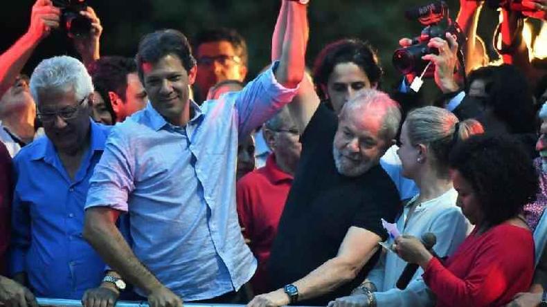 Haddad e Lula levantando os braos juntos, rodeados por outras pessoas em evento