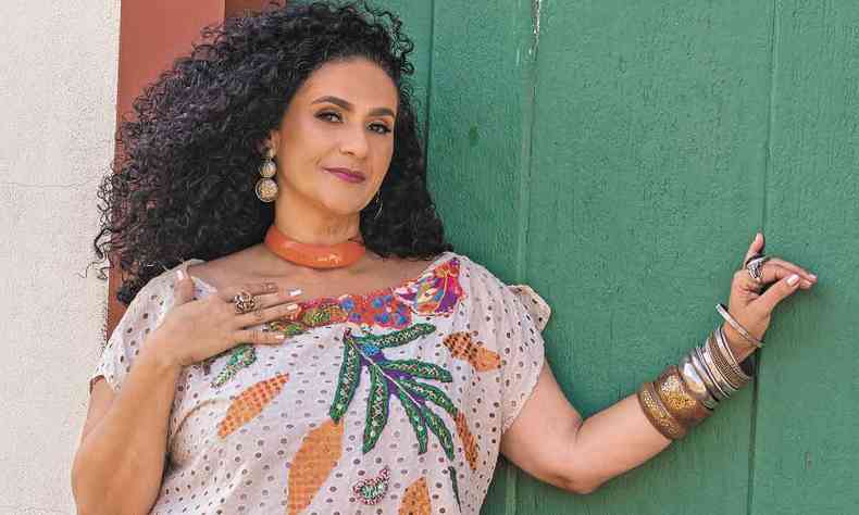 Usando vestido com bordados coloridos, Silvia Gomes olha para a cmera, recostada em porta de madeira pintada de verde