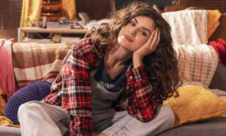 Camila Queiroz, de camisa xadrez, caracterizada como adolescente sentada no cho do quarto, em cena de %u2018de volta aos 15%u2019
