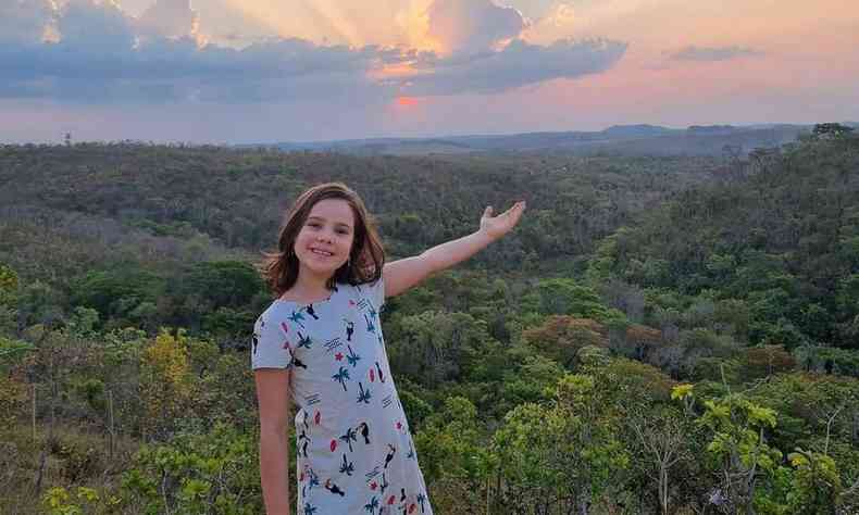 Jlia apontando para um vale, com muitas rvores ao fundo e o por do sol