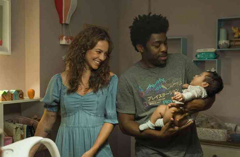 Paolla Oliveira sorri enquanto observa bebê nos braços de Lázaro Ramos, em quarto de bebê, em cena de Papai é pop