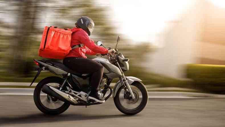 pessoa dirige moto com mochila de entrega de alimentos