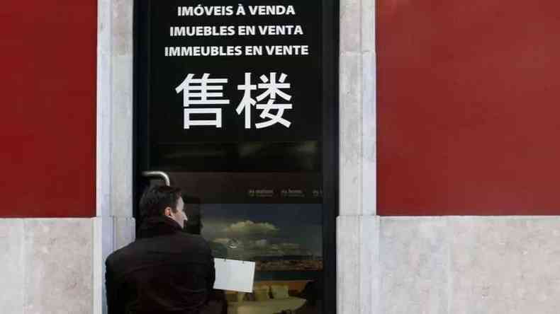Fotografia de letras em fachada dizendo 'imveis  venda' em diversos idiomas, incluindo em caracteres chineses