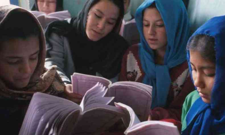 Meninas do Oriente Mdio utilizam tecidos que cobrem seus cabelos enquanto olham para livros. Elas esto agrupadas e sentadas no cho.