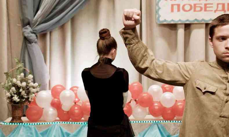 Homem ergue o brao com a mo fechada, em sinal de protesto, no filme Mariupolis. Ao fundo h mulher de costas e bales brancos e vermelhos sobre a mesa