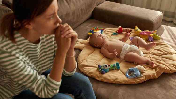 Mulher com olhar angustiado ao lado de beb deitado em sof com brinquedos