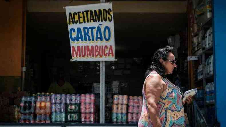 Mulher passa em frente a comrcio com placa dizendo 'Aceitamos carto Mumbuca', moeda social do programa de renda bsica do municpio de Maric (RJ)