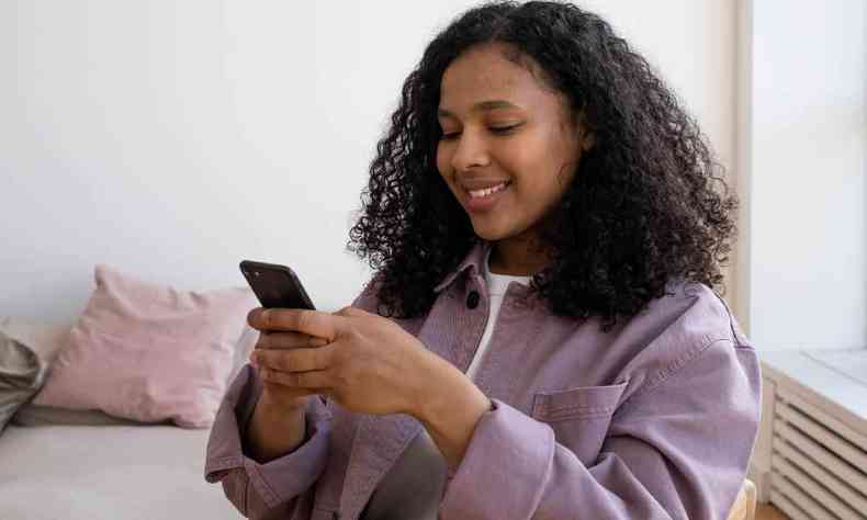 Jovem negra, usando moletom lilás, mexendo no celular 