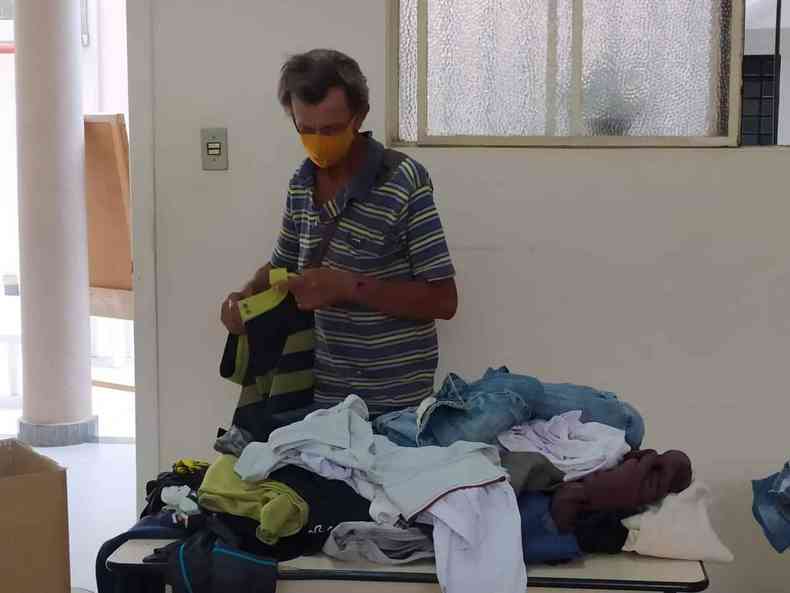 Homem escolhe agasalhos e blusas em uma mesa com muitas roupas