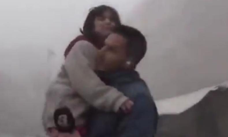Homem segura uma menina no colo saindo de escombros. Ele tem um microfone em uma das mos e um ponto de retorno no ouvido.