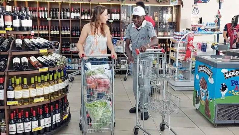O idoso conversa com cliente enquanto recolhe os carrinhos do supermercado.