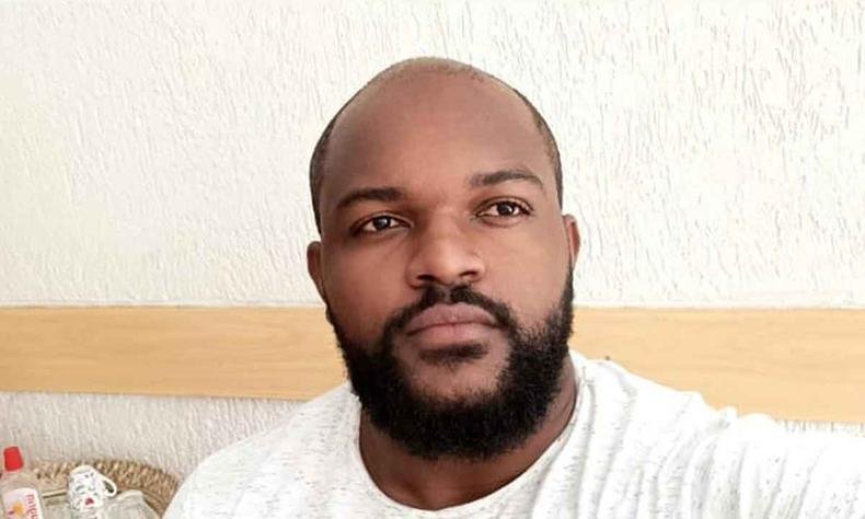 Homem negro e careca com barba e blusa branca tira uma selfie